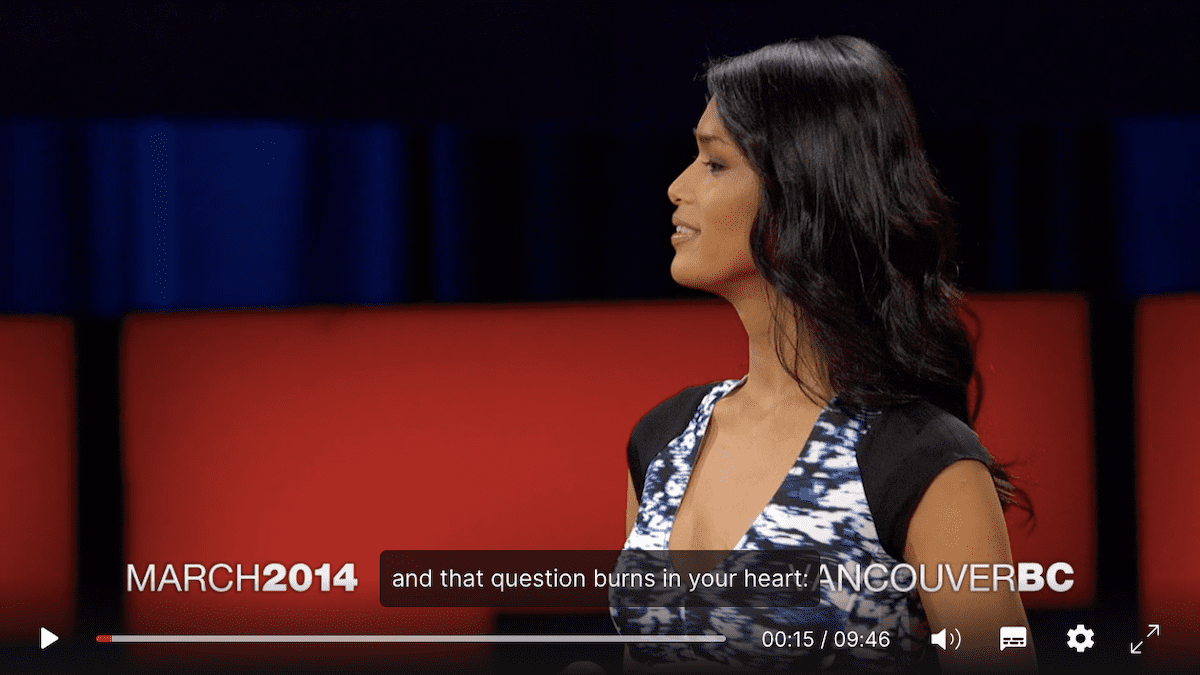 Geena Rocero giving her TED Talk. She has long hair, is wearing a dress, and is smiling. The caption is 'and that question burns in your heart.'